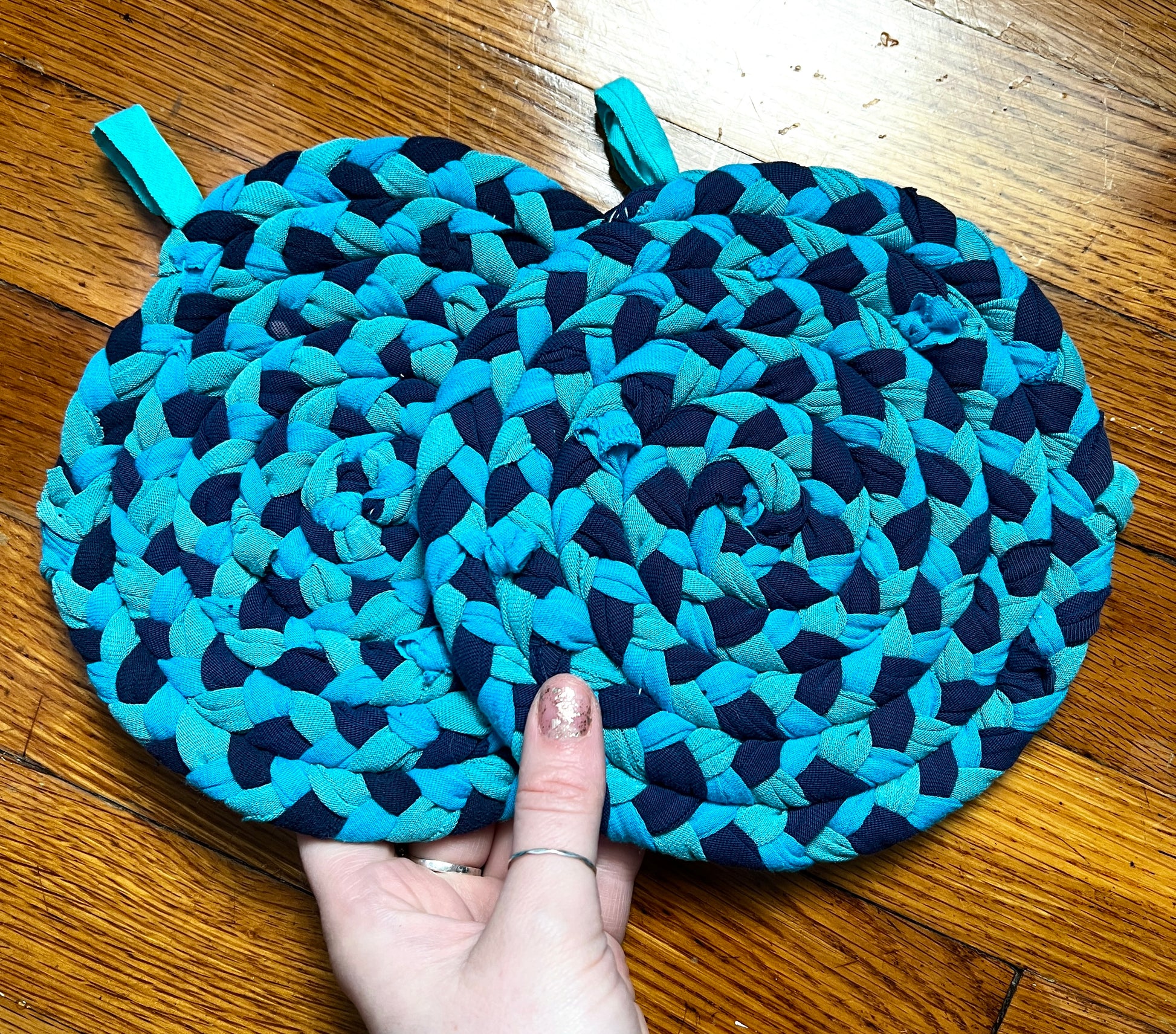 a set of two potholders, held by a hand for scale