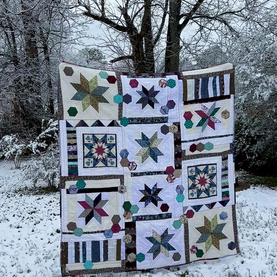 A quilt with eight point stars and quilted hexies, In a snowy outdoor scene, as the camera looks on from a distance and then gets closer