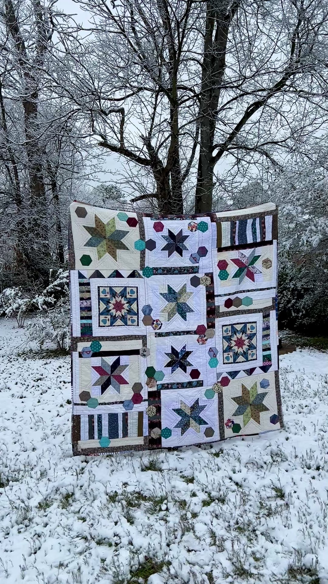 A quilt with eight point stars and quilted hexies, In a snowy outdoor scene, as the camera looks on from a distance and then gets closer