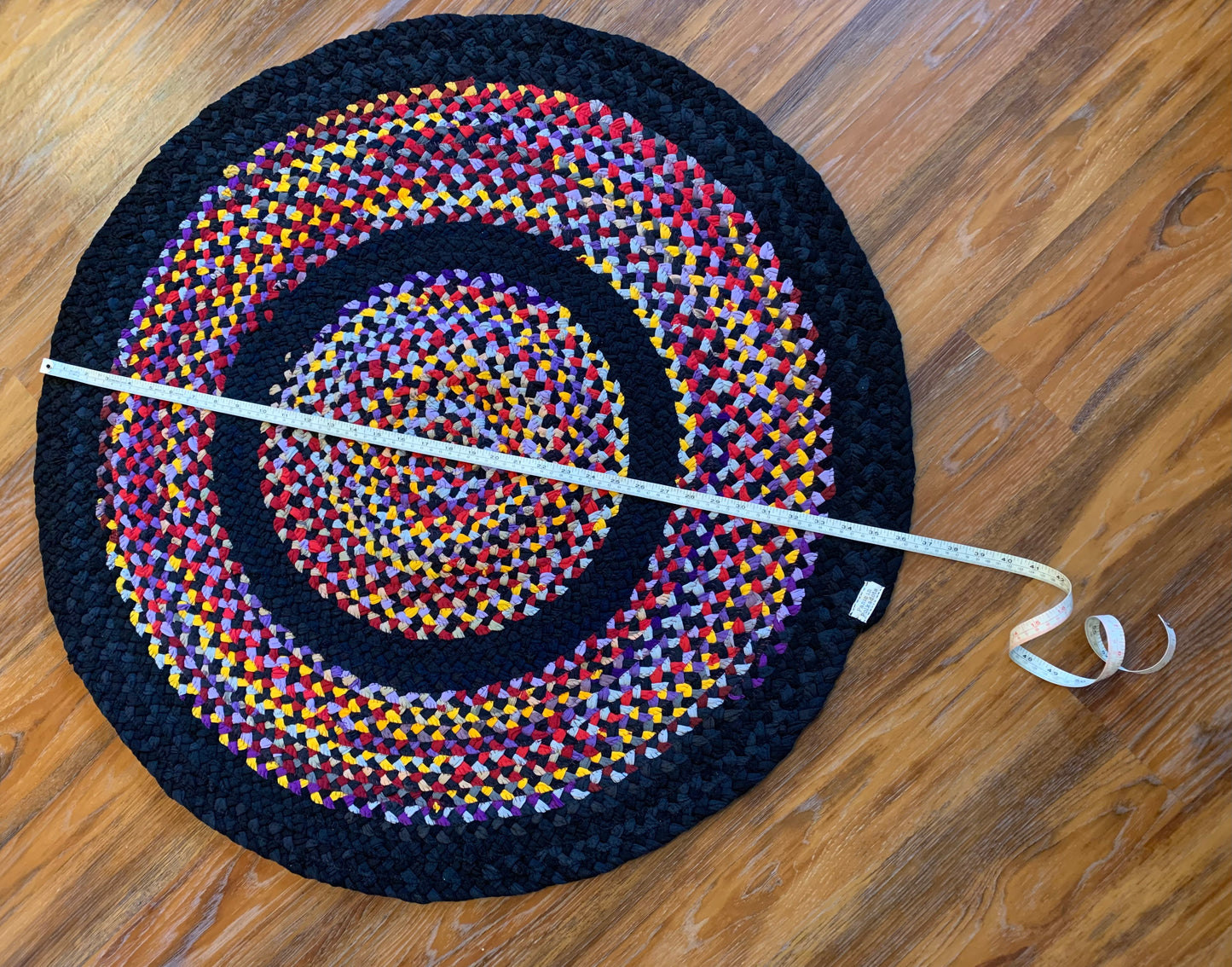 aerial view of rug, with measuring tape across it, on a wood floor background