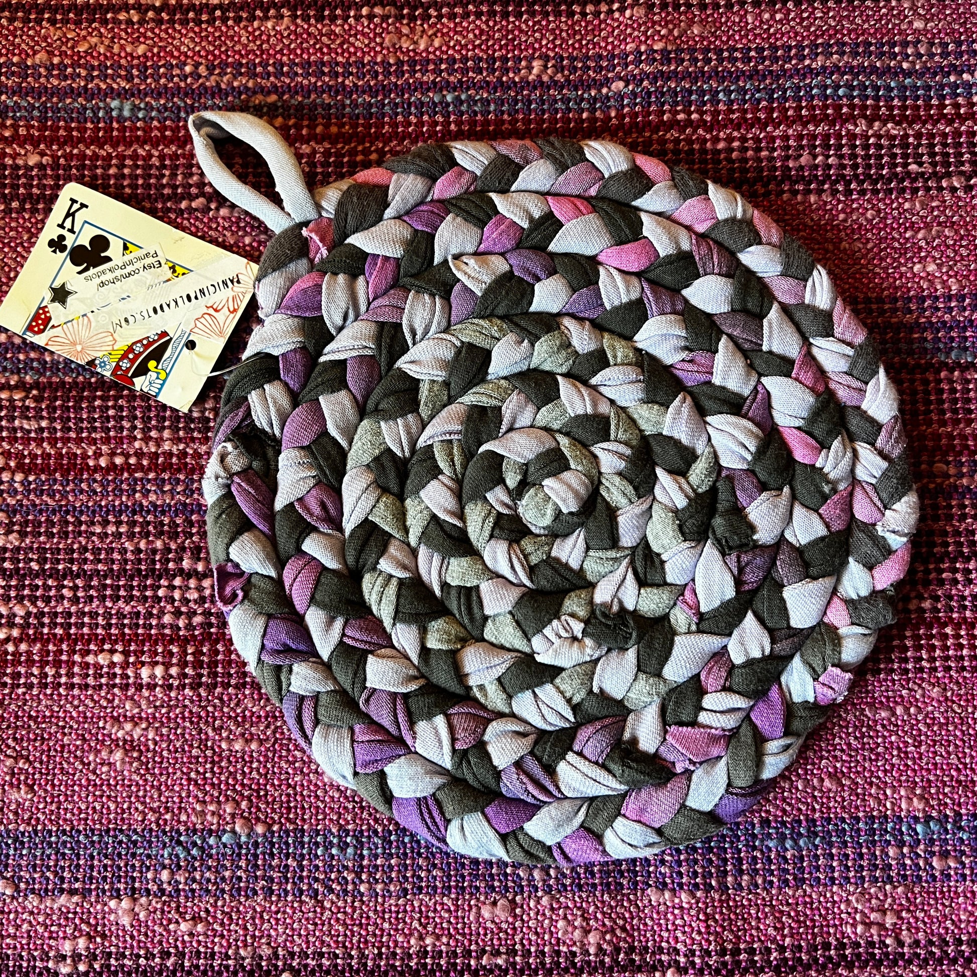 single hand braided and hand sewn potholder/trivet lay flat against a bright pink background