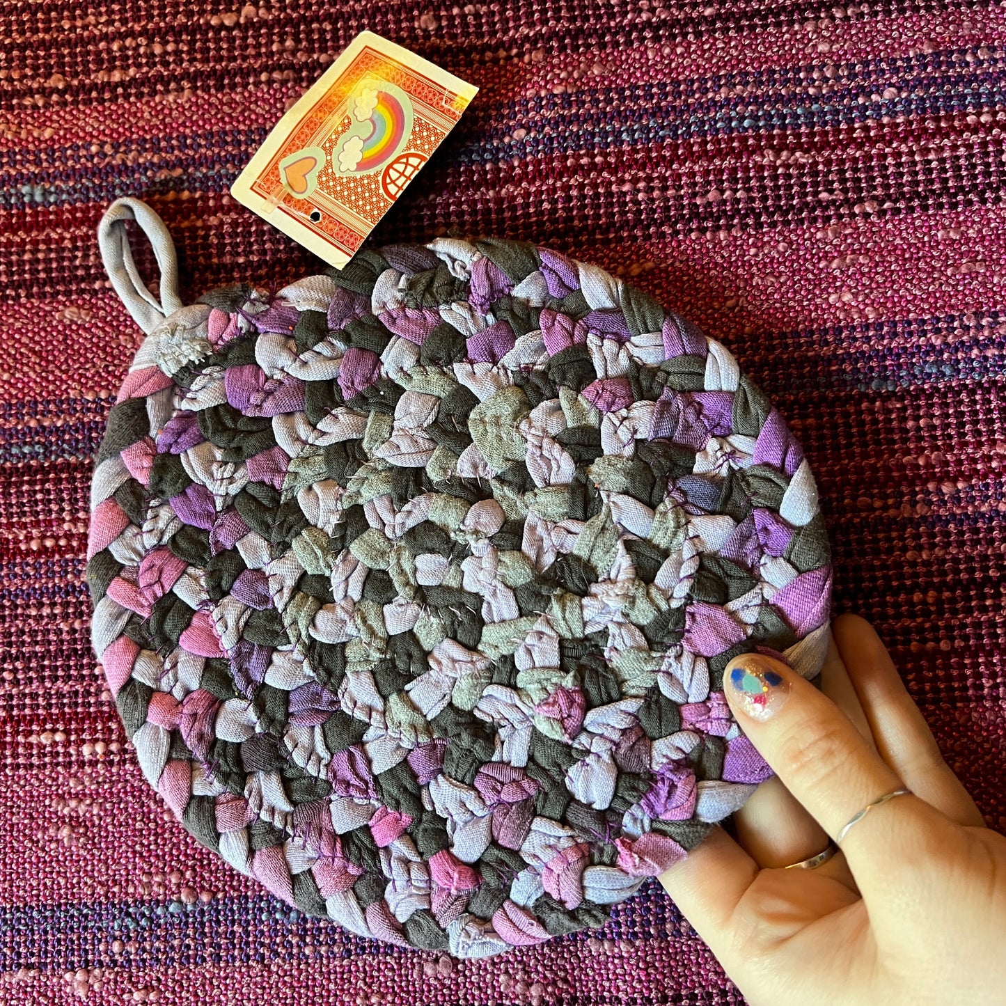 single hand braided and hand sewn potholder/trivet held up against a bright pink background