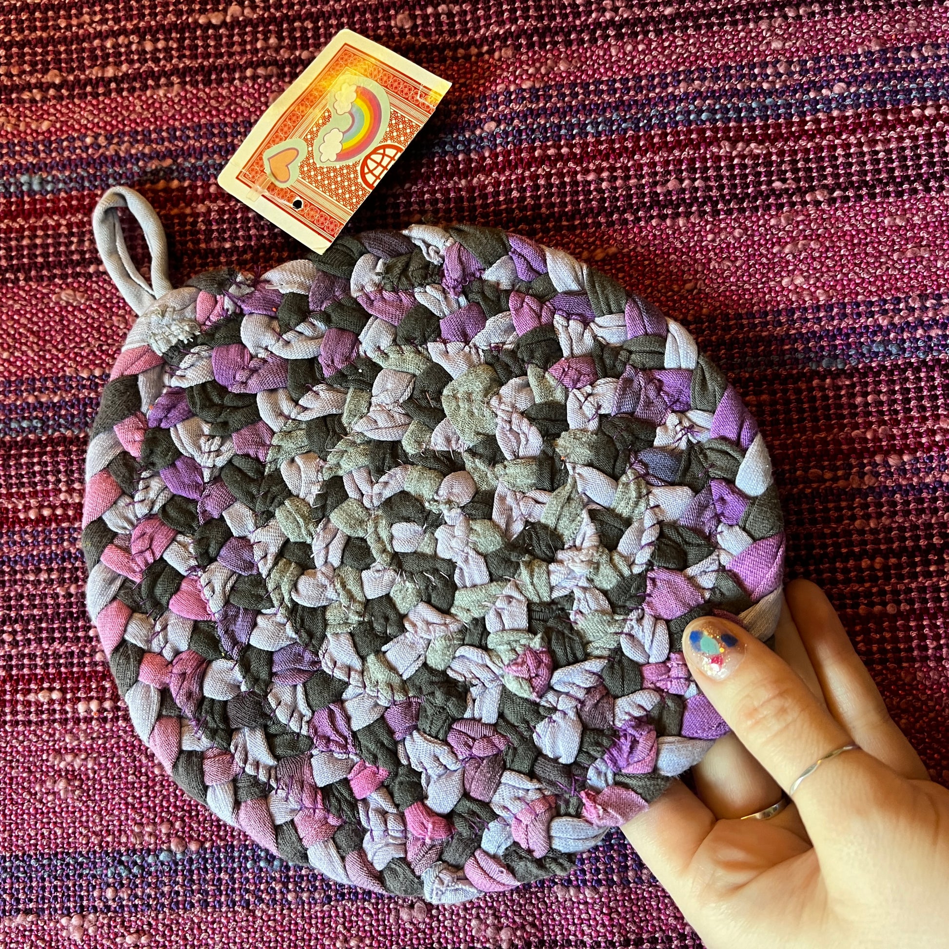 single hand braided and hand sewn potholder/trivet held up against a bright pink background