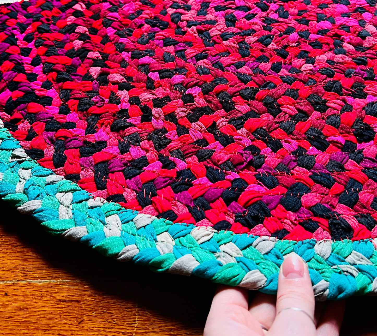 watermelon rug, hand for scale, against a wood background