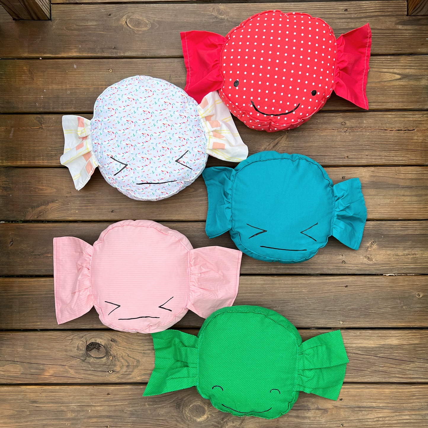 A colorful group of wrapped-candy style pillows, arranged in a zig zag column, against a wood background